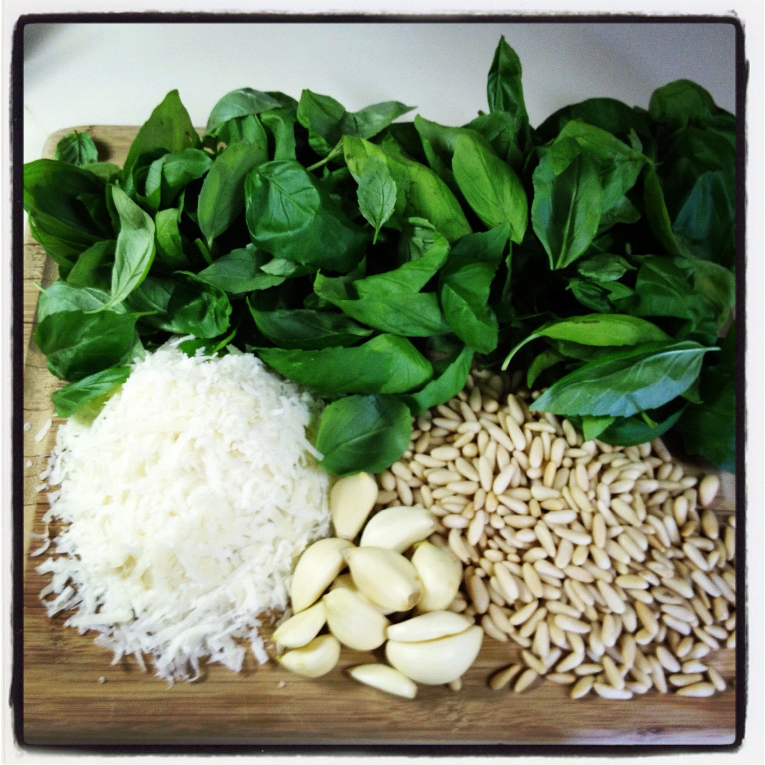 Cutting board piled high with fresh basil, pine nuts, garlic and grated cheese to be made into fresh pesto.