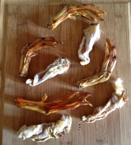 Dried rabbit ears and duck feet lie on a wooden cutting board.